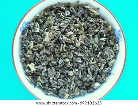 Organic green tea in a bowl on blue background. Close up, top view