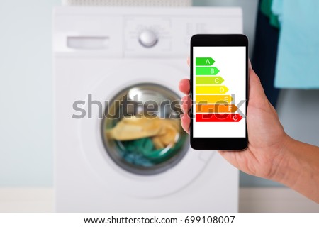 Closeup of man's hand using energy label on mobile phone against washing machine at home