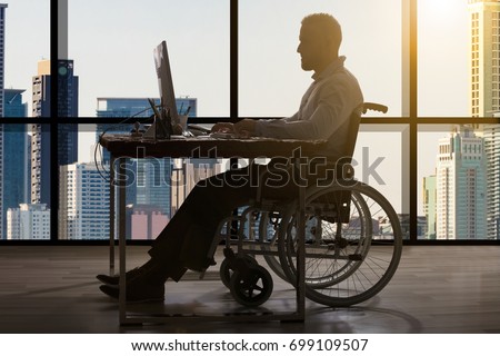 Disabled Businessman Sitting In Wheelchair Using Computer At Workplace Royalty-Free Stock Photo #699109507
