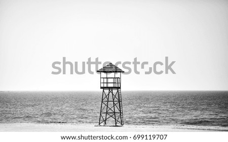 Black and white picture of a lifeguard tower on an empty beach.
