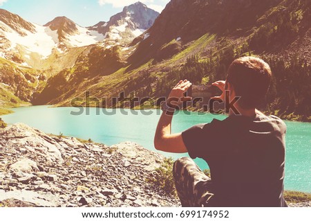 Tourist man taking picture with her smartphone in beautiful Mountain Lake in altai. Tinted instagram photos
