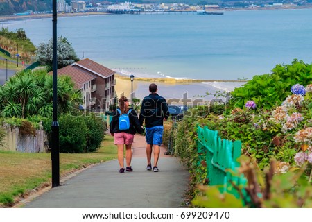 Young man and woman holding hands walk down the street leading to the sea; Isle of Wight; UK