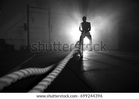 Silhouette of man working out with battle ropes at gym. Functional training. Sports and fitness concept. Royalty-Free Stock Photo #699244396
