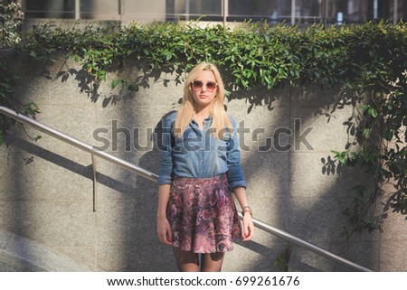 young beautiful blonde caucasian girl posing outdoor in the city wearing a jeans shirt and a floral skirt looking in camera - freshness, carefreeness, youth concept