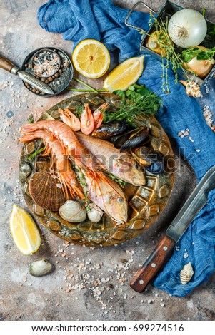 Sea fish, shrimp, clams on plate at table with lemon, knives