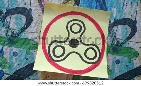 A drawing of a fidget spinner on a yellow sticky note. Warning sign.