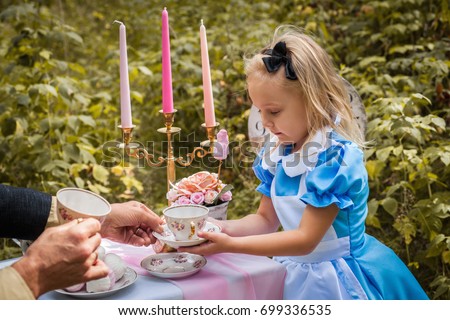 "Alice in Wonderland" styled photoshoot in forest. Girl in light blue dress drink tea with man. Royalty-Free Stock Photo #699336535