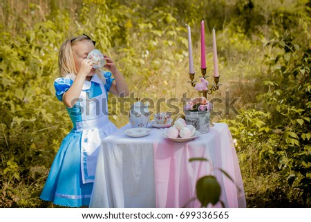 "Alice in Wonderland" styled photoshoot in forest. Girl in light blue dress drink tea. Royalty-Free Stock Photo #699336565