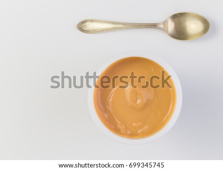 Yogurt background top view shot of caramel flavoured yoghurt in plastic cup with small silver spoon isolated on white background - close up image with space for text