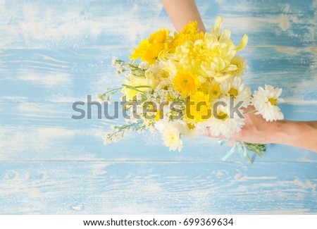 man's hand sending flowers yellow color to woman's hand on blue vintage wood background 