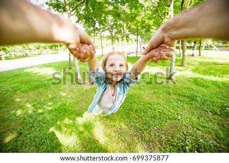 Little child being whirled by her parent over green grass in park Royalty-Free Stock Photo #699375877