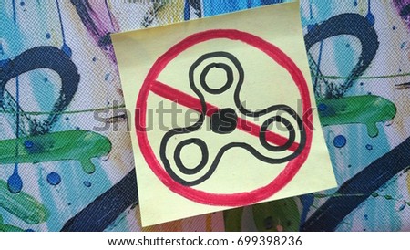A drawing of a fidget spinner on a yellow post-it note. Prohibition sign.