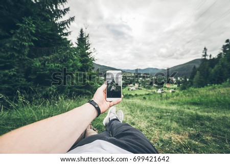 man lying on the ground and taking picture of summer mountains
