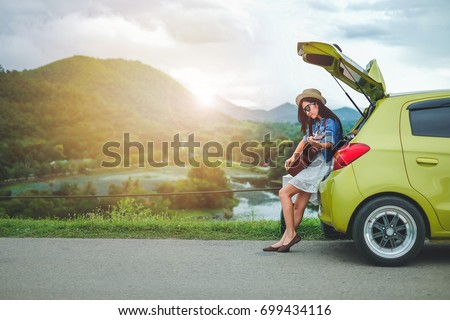Woman tourist sitting on hatchback car and playing guitar  background is mountain.Asia traveler young girl enjoying on holiday.