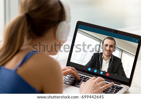 Man and woman in headphones communicating online by video call, looking at full screen videoconferencing app window, webcam videochat, virtual dating, long distance relationships, close up rear view Royalty-Free Stock Photo #699442645