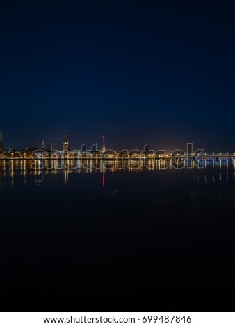 city light reflections over water at the night. colorful panorama of Riga, Latvia - vertical, mobile device ready image