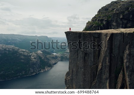 Nature photographer tourist with camera shoots while standing on top of the mountain. Beautiful Nature Norway Preikestolen or Prekestolen. Royalty-Free Stock Photo #699488764