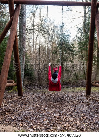 young woman in red dress using swings in spring forest having fun - vertical, mobile device ready image