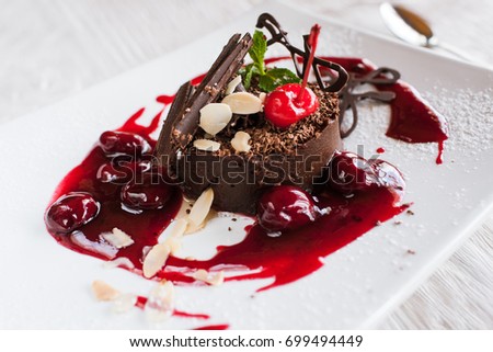 Chocolate cake on white plate with decoration from cherry, almond and mint. Delicious dessert serving in restaurant