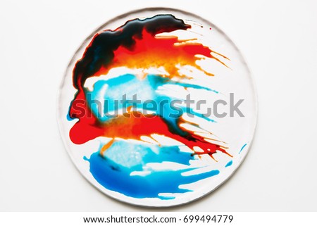 Abstract image of colorful spatters on white round plate. Watercolor blots of bright orange, red, deep brown and turquois colors flowing each other on surface