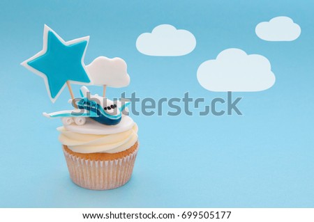 Cupcake for boy with whipped cream, decorated plane, toppers star and cloud on blue background. Picture for a menu or a confectionery catalog.