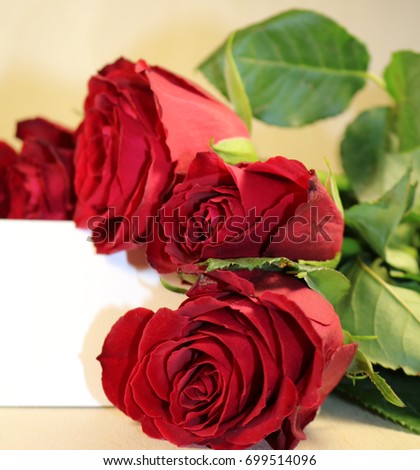 A bouquet of dark red roses with a white blank label on a wooden background
