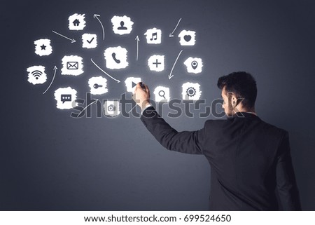 Young businessman in black suit standing in front of white multimedia icons
