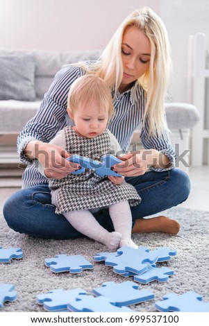 Beautiful woman and her baby playing with puzzle pieces while sitting on a carpet in the living room
