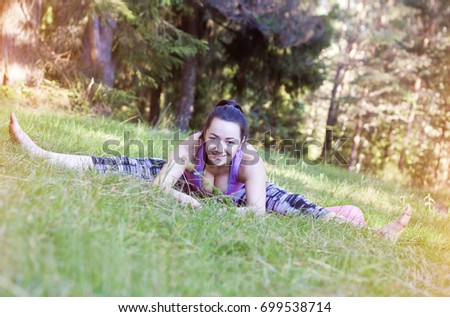 Beautiful young woman doing yoga exercises on grass in the forest at the day time. People having fun outdoors. Concept of friendly family and of summer vacation.