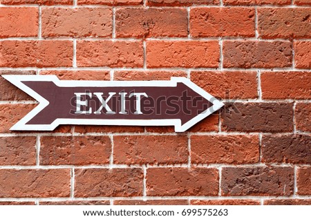 A sign beside brick walls tell the exit. Arrow symbol