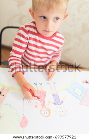 Cute child draws a house and family on paper, a blank sheet on a table