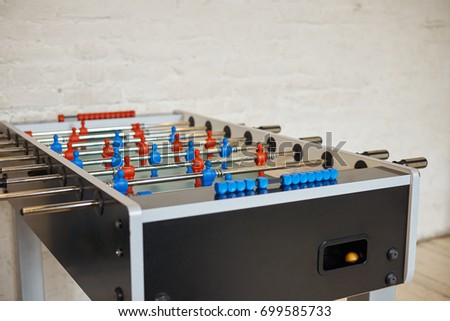 Detailed close up picture of football table with metall rods with red and blue foos men players figures in empty room with white blank copyspace wall for your advertisement or promotional content