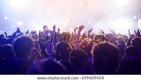 Crowd at concert - Cheering crowd in front of bright colorful stage lights Royalty-Free Stock Photo #699609454