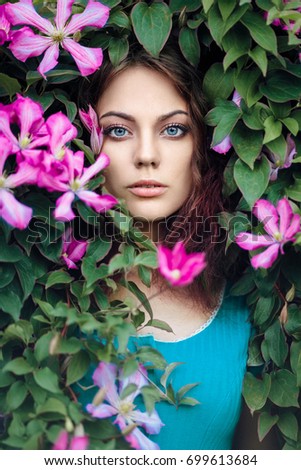 Portrait of young beautiful blue-eyed woman with purple clematis flowers around her face. Perfectly retouched.