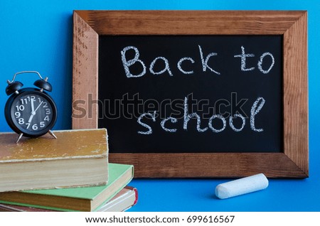 Back to school concept with stationery. School supplies on blue background. Frase Back to school written on blackboard with books, clock and piece of chalk.