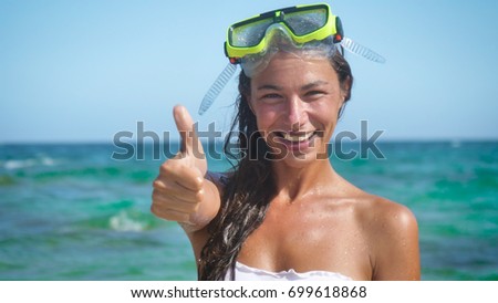 Beautiful young woman smiles at the sea, happy in a swimsuit wearing a diving mask.