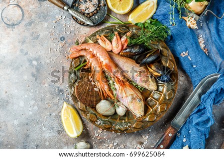 Picture of fish, shrimp, shellfish on ceramic plate at table with lemon, knives, shells