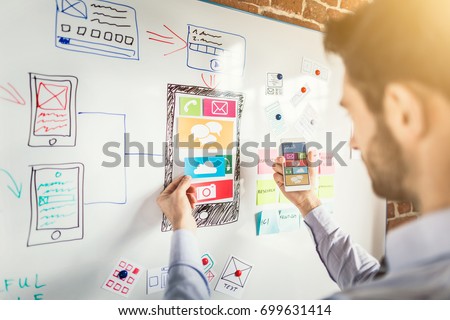 Designer man drawing website ux app development and holding smart phone on hand. User experience concept. Royalty-Free Stock Photo #699631414