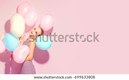 Beauty girl with colorful air balloons laughing over pink background. Beautiful Happy Young woman on birthday holiday party. Joyful model having fun, playing and celebrating with pastel color balloon