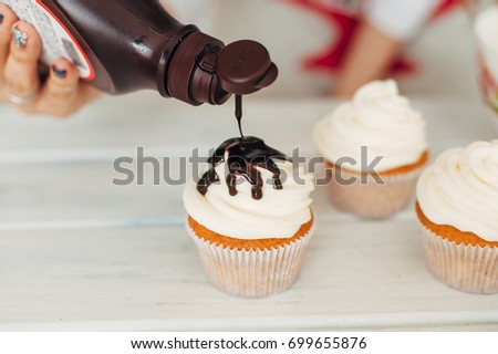 A young girl decorates cupcakes by pouring chocolate cream. Homemade food. Toning
