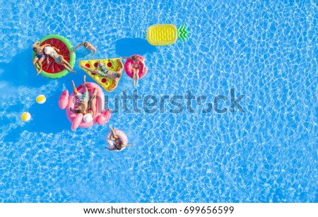 AERIAL: Group of happy attractive people hanging out on fun floaties in the pool Royalty-Free Stock Photo #699656599