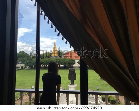 Silhouette female traveler against Bright sky with grass field in Nan Museum infront of golden pagoda in Wat Phra That Chang Kham, Nan,Thailand
