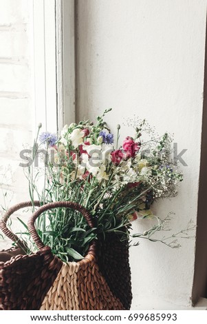 wildflowers in wicker bag on rustic white window. colorful flowers in brown basket in sunlight, space for text. rural atmospheric moment. unusual summer picture