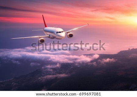 Passenger airplane. Landscape with big white airplane is flying in the red sky over the clouds and sea at colorful sunset. Passenger aircraft is landing at dusk. Business trip. Commercial plane.Travel Royalty-Free Stock Photo #699697081