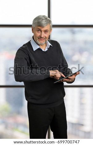 Mature man using computer tablet. Senior entrepreneur working on digital computer tablet with index finger on office window background.