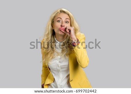 Blonde young woman making funny lips. Young business woman making funny grimace with her lips standing on grey background.