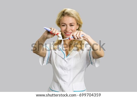 Cheerful girl applying toothpaste on toothbrush. Young beautiful female, smiling and preparing for brushing her teeth on grey background.