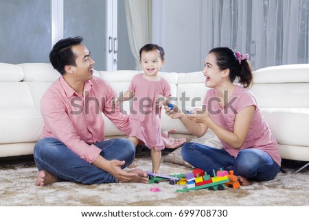 Picture of happy parents and cute girl playing with toys  while sitting at home