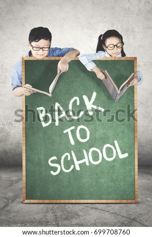 Picture of two students looks serious while reading books behind a text of back to school on the chalkboard