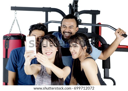Diverse people using a mobile phone to take a selfie picture together while doing a workout with weight machine